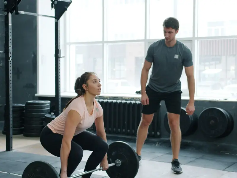 Woman set up over a loaded barbell, chest up and arms straight, with her coach watching