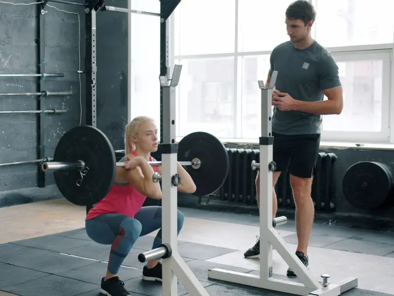 Woman front squatting out of a squat stand while a coach watches her position